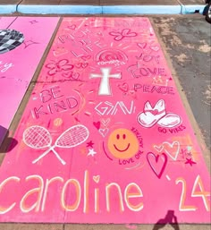 two pink signs on the sidewalk with writing written in white and black, one has a tennis racket