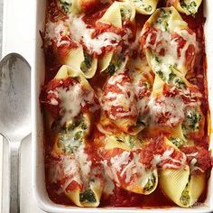 a white casserole dish filled with pasta and sauce covered in spinach leaves