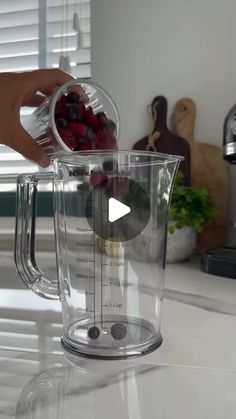 someone is mixing berries in a blender on the kitchen counter with a measuring cup