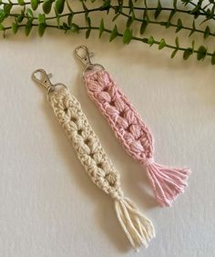 two crocheted keychains with tassels on them sitting next to a plant