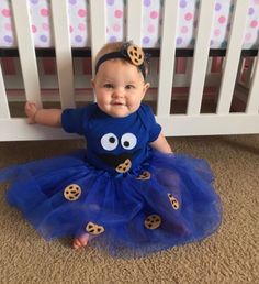 a baby girl wearing a blue dress with cookies on it's chest and smiling at the camera