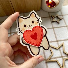 a person holding up a sticker with a cat on it's back and a heart in the middle