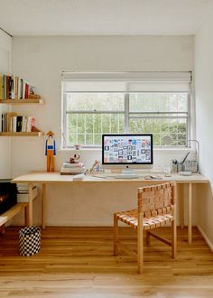 a desk with a computer on top of it in front of a window next to a wooden chair