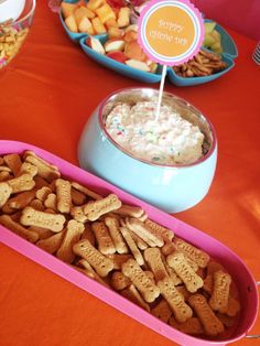 a table filled with bowls and trays of crackers on top of an orange table cloth