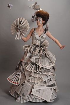 a woman in a dress made out of newspapers and holding a fan with her right hand