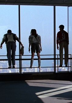 three people standing in front of large windows looking out at the city below and holding their hands together