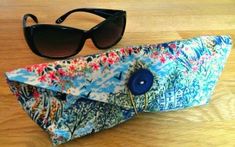 a pair of sunglasses sitting on top of a blue and white bag next to a pair of black sunglasses