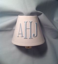 a lamp shade that has the letters ahj on it and is sitting on a bed