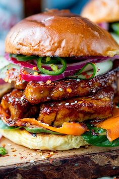 a chicken sandwich with onions, carrots and lettuce on a wooden cutting board