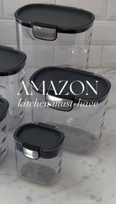 four clear storage containers with black lids on a marble countertop