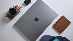 an apple laptop computer sitting on top of a white desk next to a camera and notebook