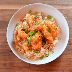 a white bowl filled with rice covered in meat and green onions on top of a wooden table