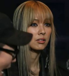 a woman with long blonde hair wearing a black hat and leather jacket is talking to someone