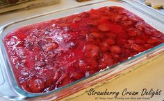 a glass dish filled with strawberry jam on top of a wooden table next to a knife