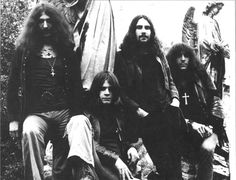 an old black and white photo of four men with long hair sitting on the ground