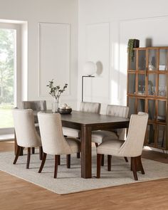 a dining room table with beige chairs and a white rug in front of the window