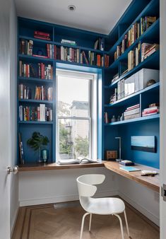 a white chair sitting in front of a window next to a book shelf filled with books