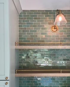 a light that is on above a shelf in a room with green tile and white cabinets