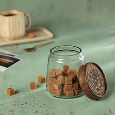 a glass jar filled with wooden cubes on top of a green table next to a cup