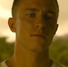 a close up of a person wearing a white t - shirt with trees in the background