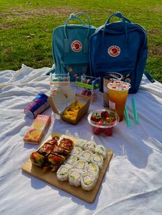 an assortment of sushi and drinks on a picnic blanket in the park with backpacks