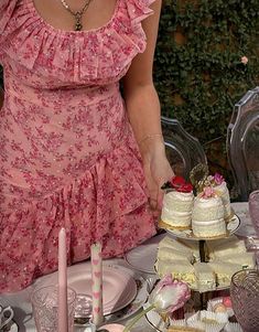 a woman in a pink dress standing over a table filled with cakes and cupcakes