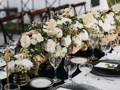 the table is set with black and white plates, silverware, and floral centerpieces