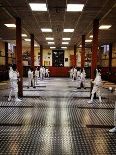 a group of men in white fencing suits practicing their moves on the mats inside an indoor gym