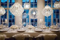 a dining room table is set up with chandeliers and candles in front of large windows