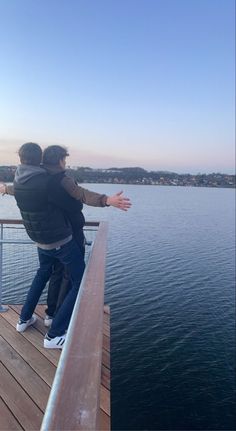 two people are standing on a dock by the water looking at something in the distance