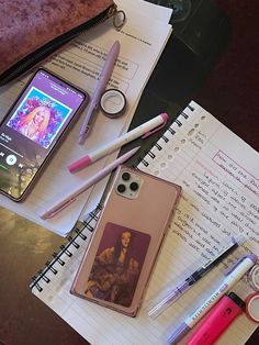 a cell phone sitting on top of a notebook next to some pens and pencils