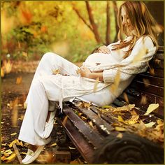 a beautiful woman sitting on top of a wooden bench in the woods with leaves all around her