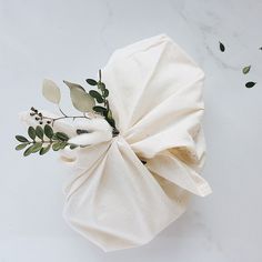 an arrangement of flowers wrapped in white paper on a marble counter top with leaves and twigs