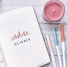 an open notebook sitting on top of a wooden table next to pens and a candle