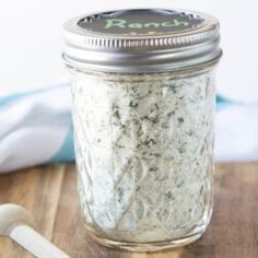 a jar filled with white stuff sitting on top of a wooden table next to a spoon