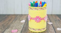 a yellow tin can filled with markers and pens on top of a wooden table next to flowers