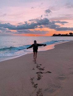 a woman is walking on the beach with her arms spread out and footprints in the sand