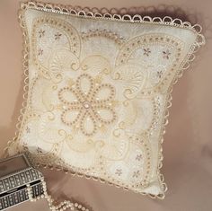 a white pillow with beading on it sitting next to a cell phone and keychain