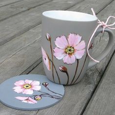 a coffee cup with pink flowers painted on it next to a coaster that has been placed on a wooden table