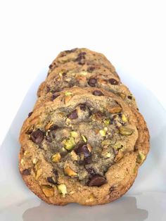 three chocolate chip cookies sitting on top of a white plate with the words dark chocolate pistachio thin cookies