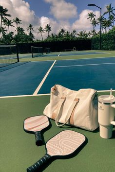 a tennis racket, cup and bag sitting on the court with palm trees in the background