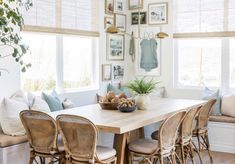 a dining room table with chairs and pictures on the wall above it in front of two windows