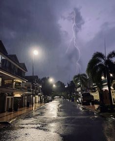 a city street at night with a lightning bolt in the sky over buildings and trees