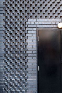 a black door in front of a brick wall with an intricate design on it's side