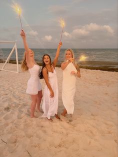 three women in white dresses holding sparklers on the beach