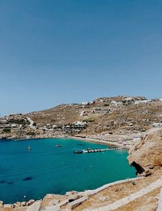 the blue water is surrounded by rocky hills and boats in the bay, with houses on the hill behind it