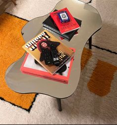 a glass table topped with books on top of a white carpeted floor next to a chair