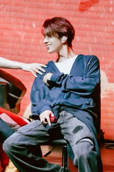 a young man sitting on top of a chair next to a red brick wall,