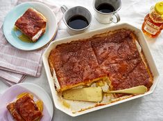 a casserole dish on a table with two cups of coffee