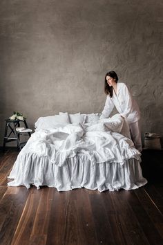 a woman sitting on top of a bed with white sheets and ruffled bedspread